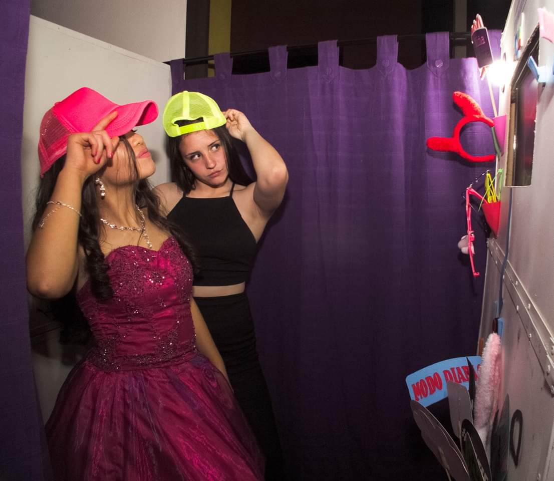 Invitadas posando con gorras divertidas junto a la fotocabina en un cumpleaños de 15